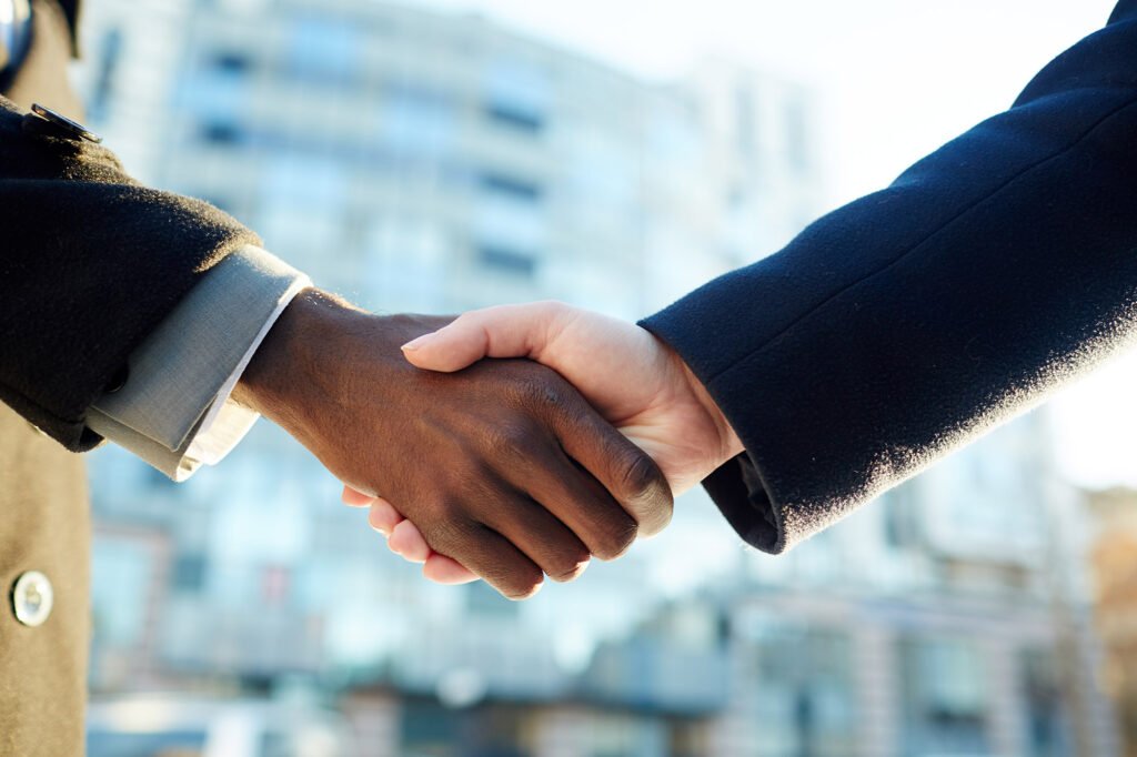 Closeup portrait of two international business partners shaking hands against office building outdoors. Male African-American hand and female Caucasian hand.